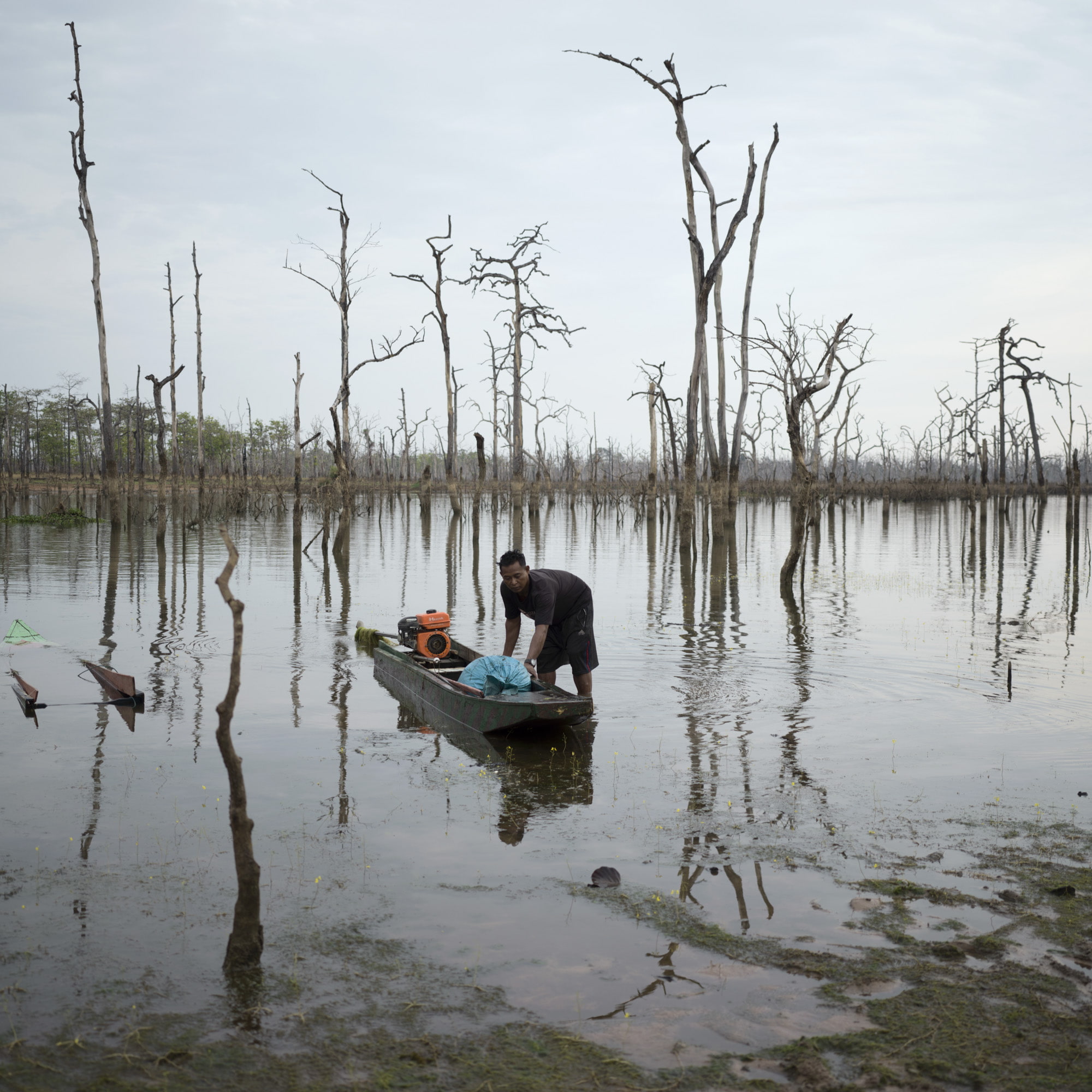Man pulling his boat to shore in a flooded forest river